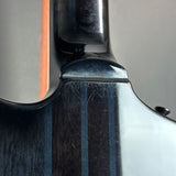 Close-up detail of a glossy black electric guitar body showing the edge of the neck joint, wood grain, and a small portion of the headstock against a neutral gray background.