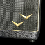 Close-up of a textured black speaker grille with two gold V-shaped metal logos on a black background.