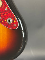 Close-up of a guitar with a red pickguard and black finish on a gray background