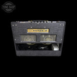 A black textured guitar amplifier head photographed from the front against a solid black background, with a gold control panel and two front speaker grilles. A Tone Shop watermark is visible in the top-left corner.