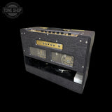 A black guitar amplifier with a textured patterned front grille, gold control panel accents, and a top carry handle, shown on a solid black background with a Tone Shop watermark in the top left corner.
