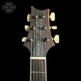 Close-up of the headstock of a McCarty Soft acoustic guitar against a black background, featuring a dark wood finish, cream tuning pegs, and a white signature on the backplate.
