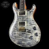 A close-up of an electric guitar body with a distressed silver-gray flamed maple top, black pickups, gold hardware, and a natural wood neck visible against a black background. A Tone Shop watermark is in the upper left corner.