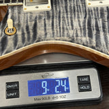 Close-up of a guitar body resting on a digital scale displaying 9.24 oz, showing the wood grain finish and hardware details.