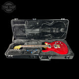 A red electric guitar with a yellow headstock sits inside an open black hard case with gray foam lining, photographed against a black background. A Tone Shop watermark appears in the upper left corner.