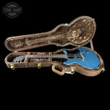 Blue electric guitar in a brown hard case with 'Tone Shop' logo.