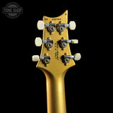 Close-up rear view of a gold-finish guitar headstock with six tuners and white tuning keys, shown against a black background. A Tone Shop watermark is visible in the upper left corner.
