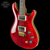 A red electric guitar with a glossy flamed maple finish, gold hardware, and a black background. A Tone Shop watermark is visible in the top left corner.