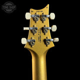 Close-up of the headstock of a gold electric guitar, showing six tuning pegs, white tuning keys, and printed serial number '0427910' on a black background.