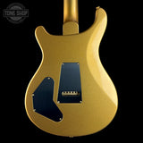 Close-up of the back of a gold electric guitar body with black pickguard plates and a visible Tune Shop watermark in the upper left corner, set against a solid black background.