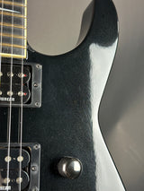 Close-up of a black electric guitar with visible wear and a metallic button.