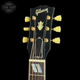 Close-up of a Gibson electric guitar headstock with a black finish, gold tuning pegs, gold hardware, and a gold Gibson logo on a black background.