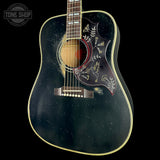A vintage-style acoustic guitar with a distressed black star-spangled body, featuring gold bird and floral inlays on the pickguard, set against a solid black background.