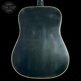 The back of a dark blue acoustic guitar with a light cream edge trim, shown against a solid black background. A Tone Shop watermark is visible in the top left corner.