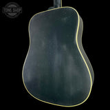 The back of an acoustic guitar with a dark, distressed black finish and a thin light-colored binding edge, shown against a solid black background.