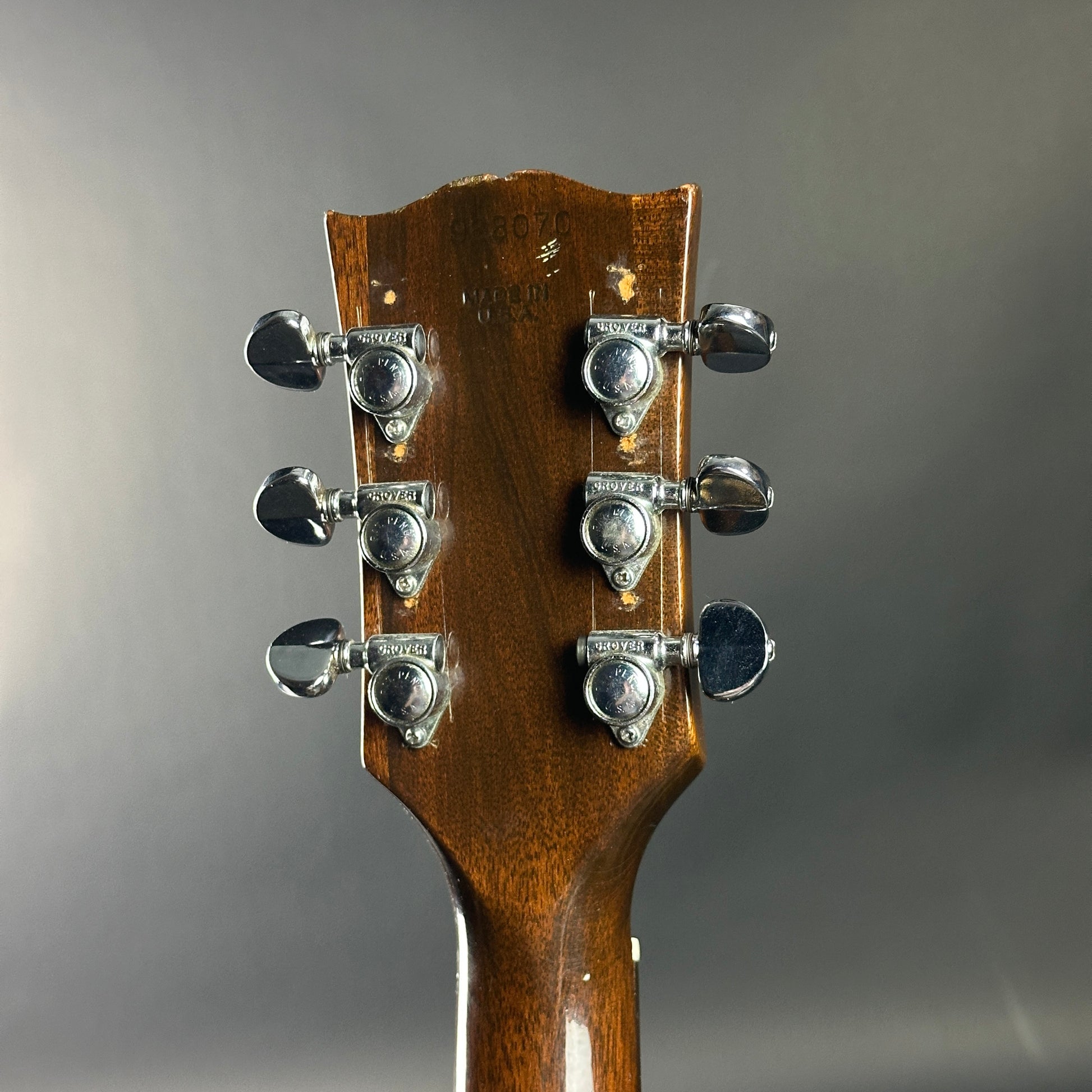 Close-up of a guitar headstock with tuning pegs on a gray background