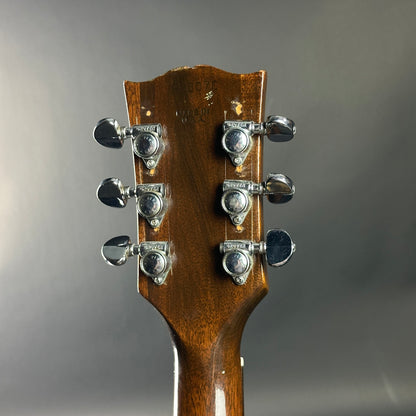 Close-up of a guitar headstock with tuning pegs on a gray background