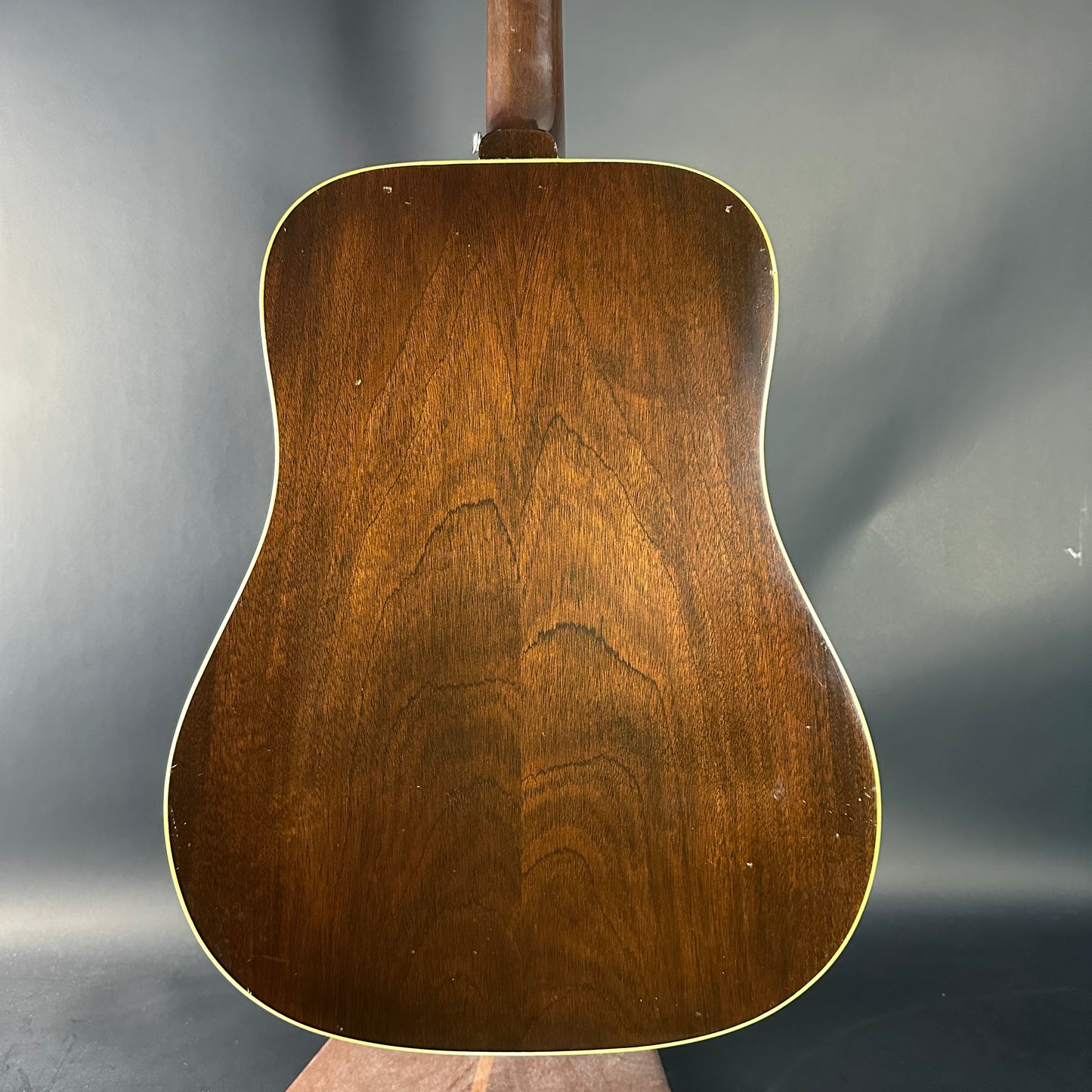 Back view of a wooden acoustic guitar on a gray background