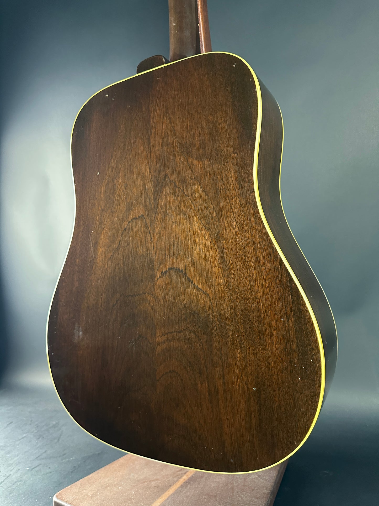 Close-up of a wooden acoustic guitar body on a reflective surface with a dark background