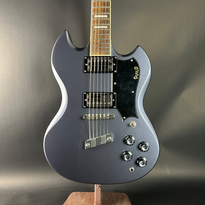 Gray electric guitar on a stand against a gray background