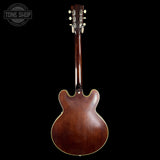 Back view of a brown electric guitar on a black background with 'Tone Shop' logo.