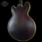 Back view of a guitar with a dark finish on a black background, featuring the Tone Shop logo.