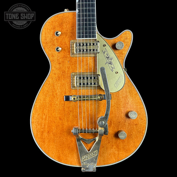 Orange electric guitar with a visible brand logo on a black background