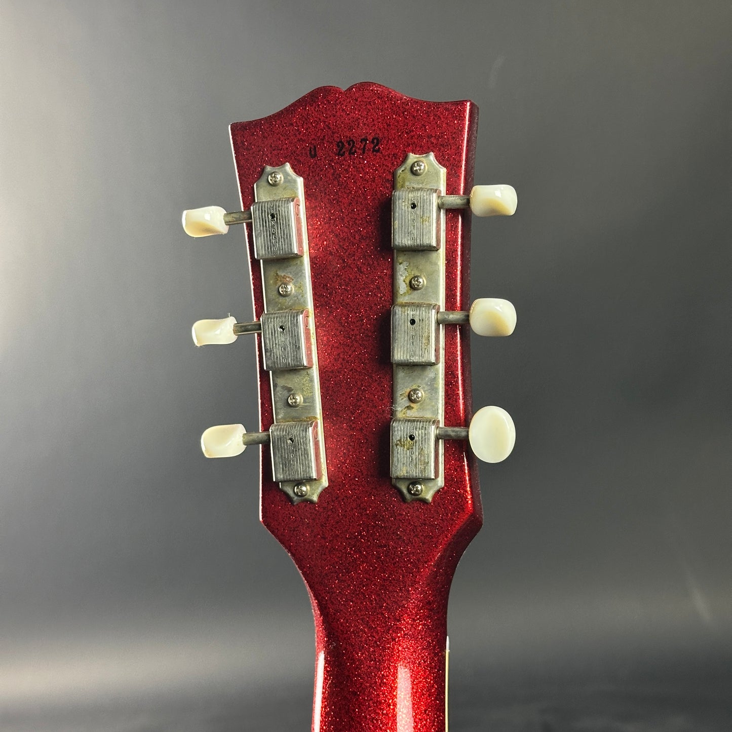 Close-up of a red guitar headstock with tuning pegs on a gray background