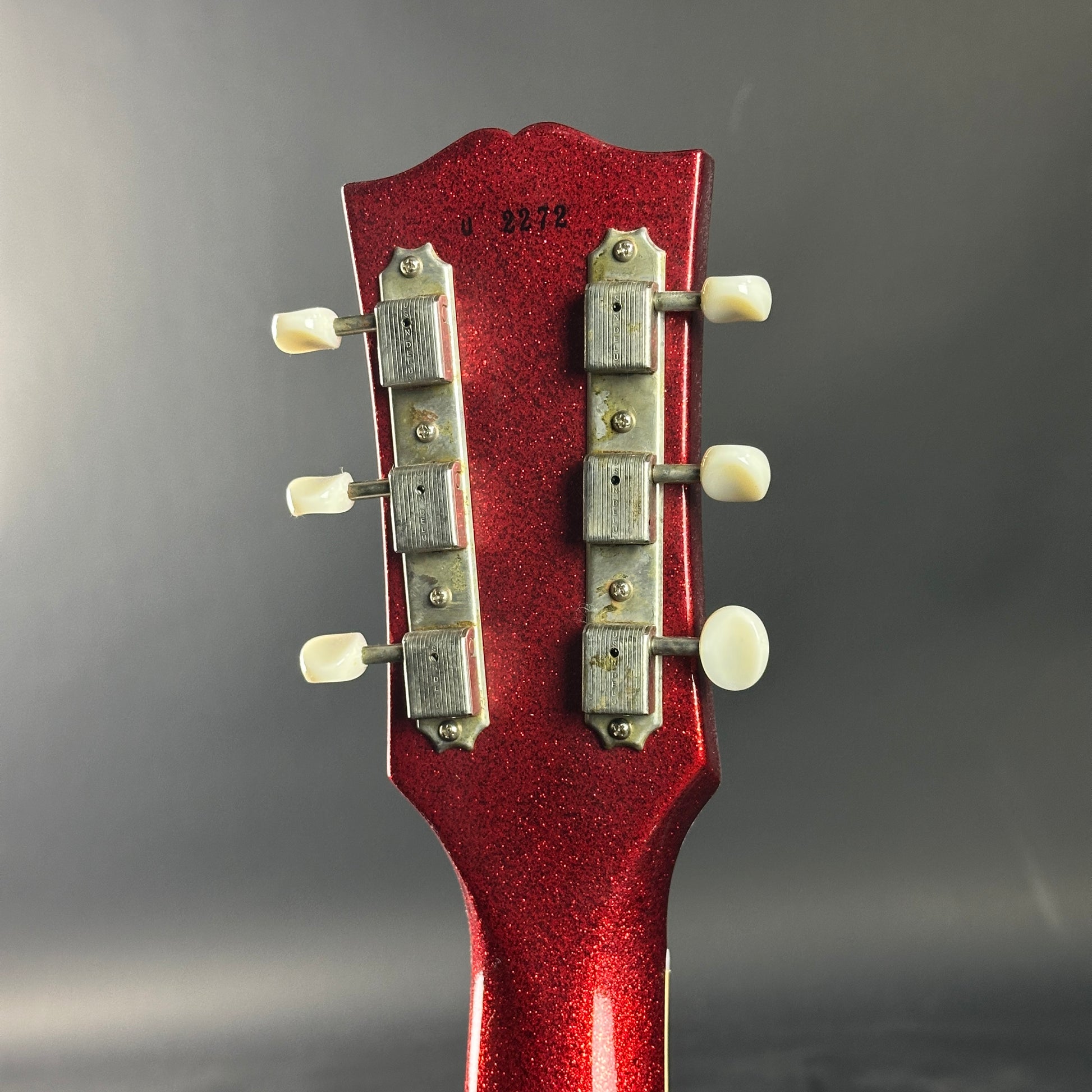 Close-up of a red guitar headstock with tuning pegs on a gray background