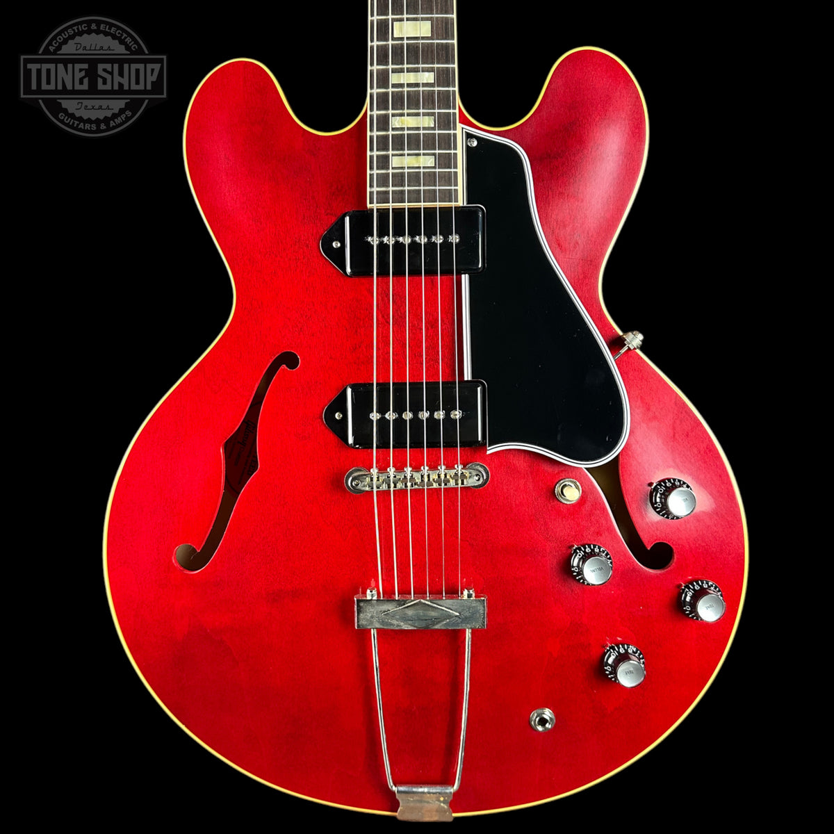 Red electric guitar with a black pickguard on a black background, featuring the Tone Shop logo.