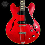 Red electric guitar with a black pickguard on a black background, featuring the Tone Shop logo.