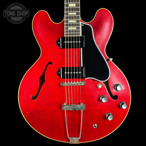 Red electric guitar with a black pickguard on a black background, featuring the Tone Shop logo.
