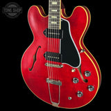 Red electric guitar with a black pickguard on a black background, featuring 'Tone Shop' logo.