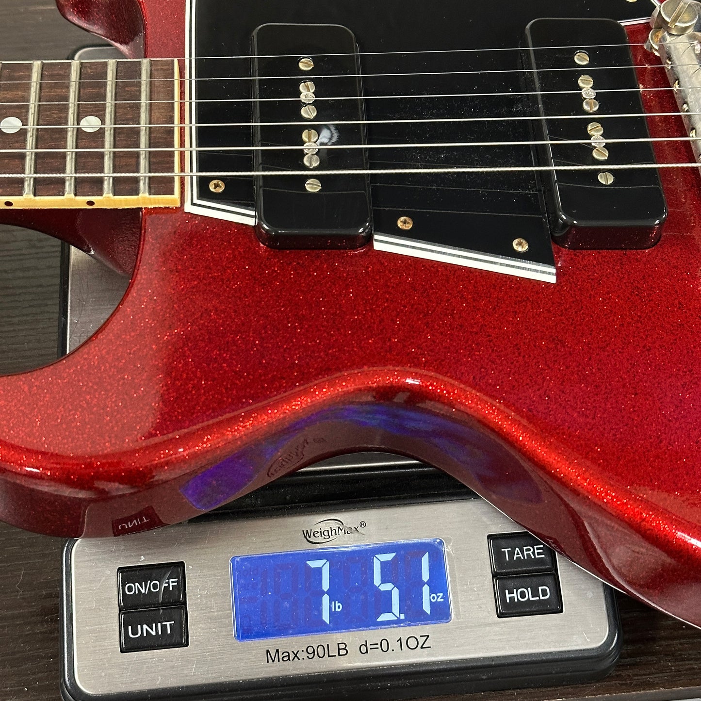 Red electric guitar on a digital scale displaying weight
