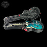 Blue electric guitar in a black case with 'Tone Shop' logo.