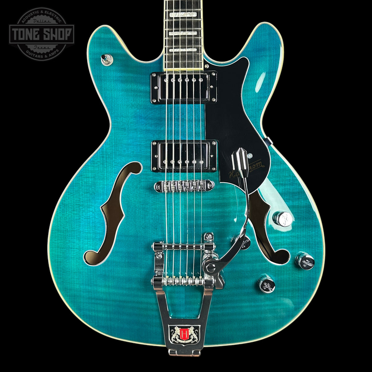 Turquoise electric guitar with a black pickguard on a black background, featuring 'Tone Shop' branding.