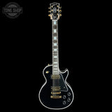 Black electric guitar with gold hardware on a black background, featuring 'Tone Shop' logo.