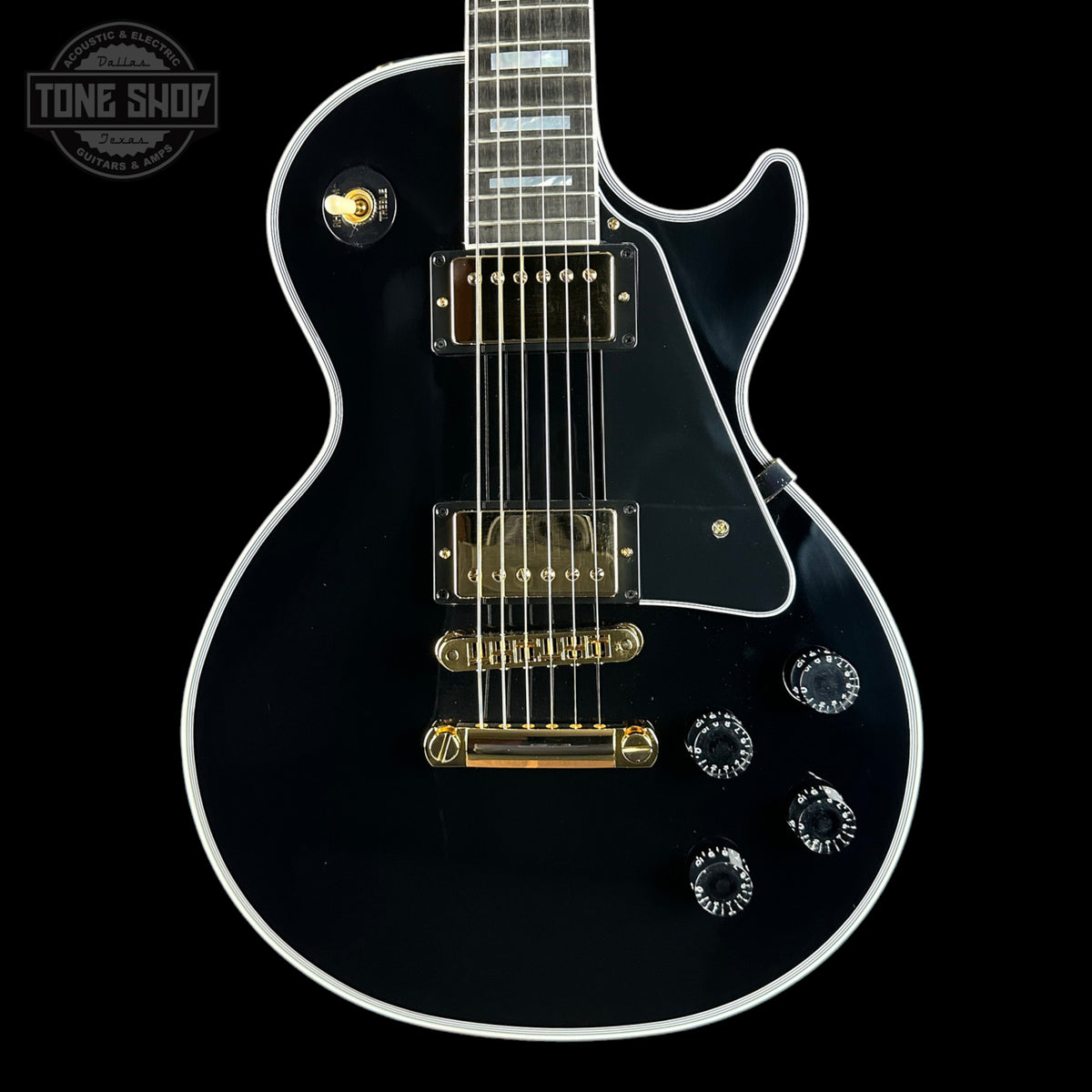 Black electric guitar with gold hardware on a black background, featuring 'Tone Shop' branding.
