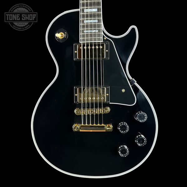Black electric guitar with gold hardware on a black background, featuring 'Tone Shop' branding.