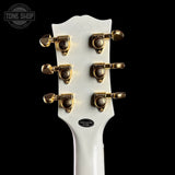 Close-up of a white guitar headstock with gold tuning pegs on a black background, featuring 'Tone Shop' branding.