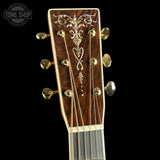 Close-up of a guitar headstock with intricate design and gold tuning pegs on a black background.