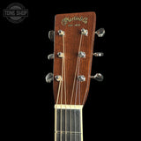Close-up of the headstock of a Martin & Co acoustic guitar against a solid black background, showing the brand name in gold script and the tuning pegs.