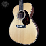 A close-up of a wooden acoustic guitar body against a solid black background, featuring a natural maple top, dark brown sides, a tortoiseshell-style pickguard, and a black bridge. A Tone Shop watermark is visible in the top left corner.