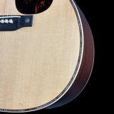 Close-up detail of an acoustic guitar body showing the natural wood grain top, sound hole, black bridge, and dark wood edge against a black background.