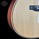 Close-up detail of an acoustic guitar body showing the natural wood grain, soundboard texture, and part of the bridge against a black background.