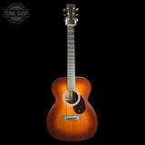 A wooden acoustic guitar with a natural sunburst finish, shown from the front against a solid black background. A Tone Shop watermark is visible in the top-left corner.