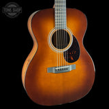 A close-up of an acoustic guitar body showing a natural sunburst finish that fades from bright orange to dark brown, with a silver bridge and soundhole rosette, set against a solid black background.