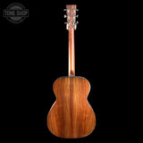 The back view of a wooden acoustic guitar, showcasing its rich grain and six tuning pegs, set against a solid black background with a Tone Shop logo in the top left corner.