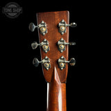 Close-up of the headstock of a wooden acoustic guitar, showing six tuning pegs with ornate gold-toned hardware against a black background. A Tone Shop watermark is visible in the top left corner.