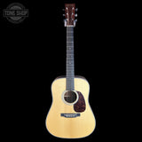A natural wood acoustic guitar with a dark headstock and black pickguard, shown vertically against a solid black background. A Tone Shop watermark is visible in the top-left corner.